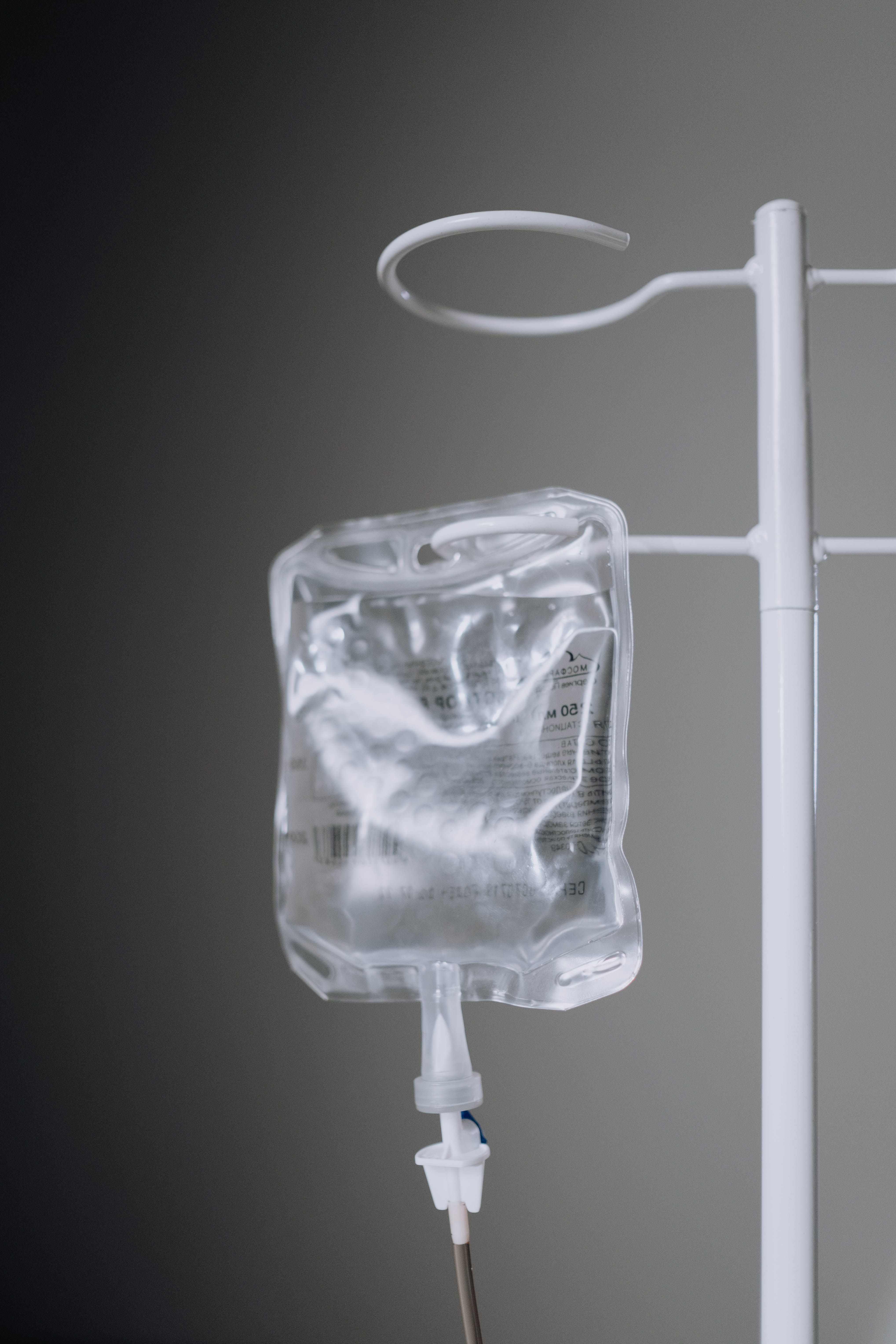A clear IV fluid bag hanging from a rolling stand against a softly lit gray background