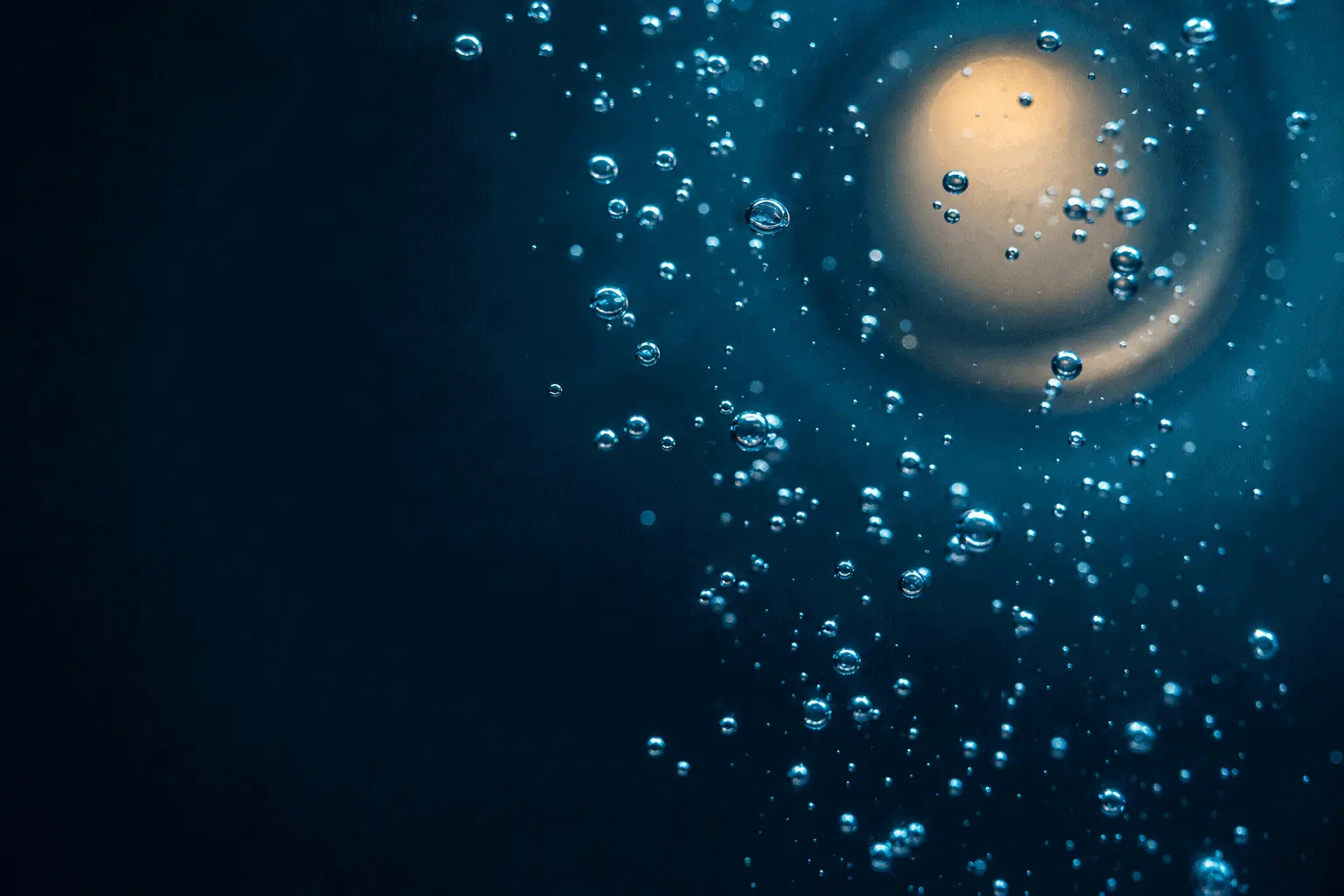 Oxygen bubbles rising through deep blue water toward a warm porthole light